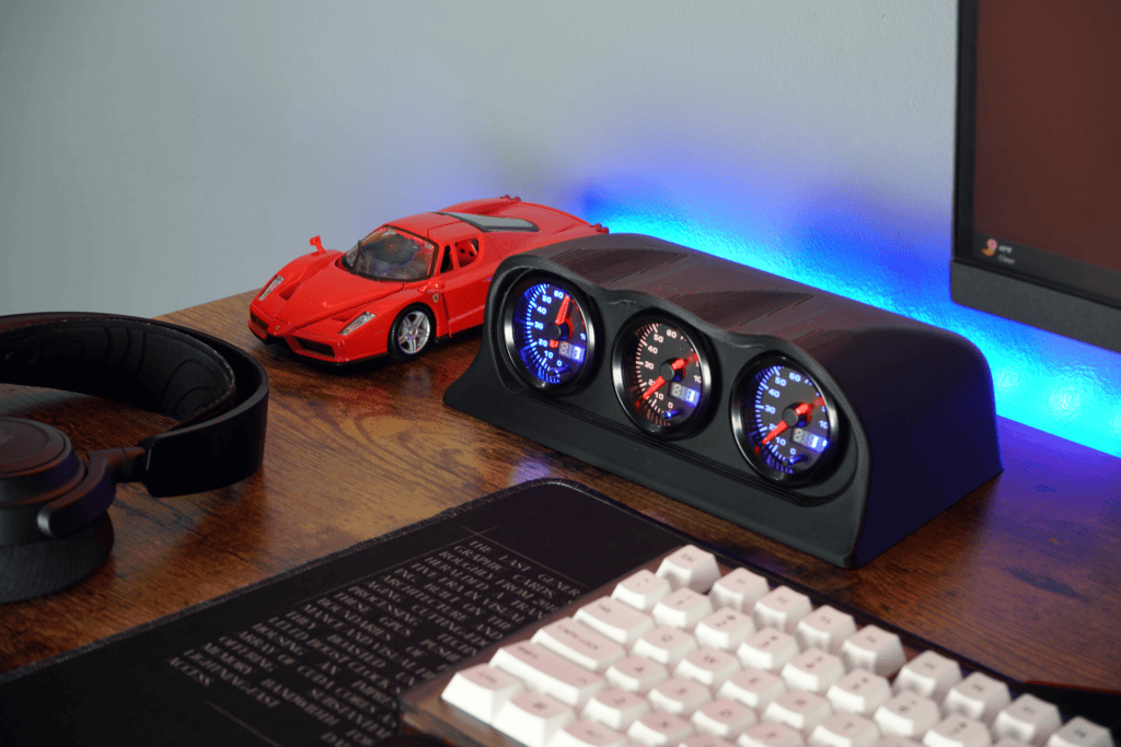Tech desk setup with Lumen Dash, a sleek dashboard with analog gauges, a red model car, and gaming accessories for a modern workspace.
