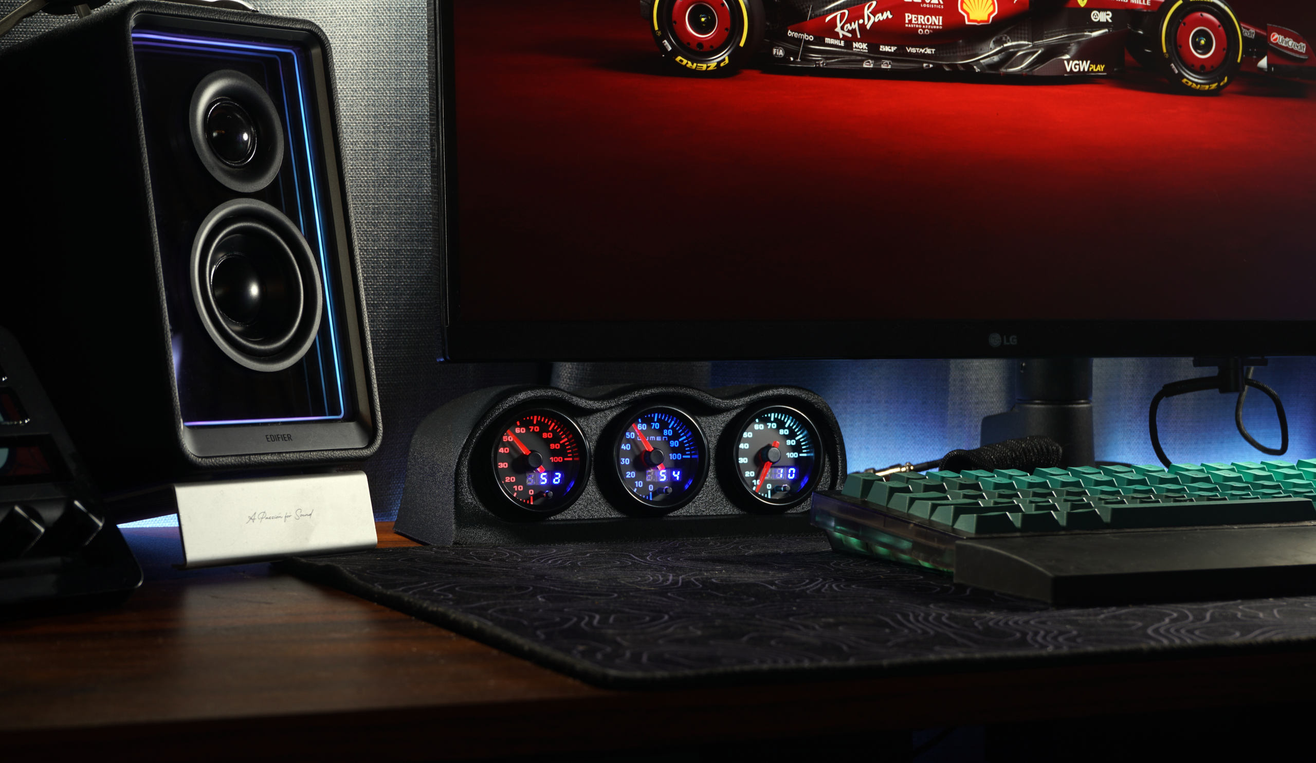 Gaming monitor, speakers, and gauges on a desk setup.